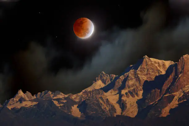 A total lunar eclipse with the red Moon at night in misty clouds over Himalayan mountains, the Himalayas, Uttarakhand, India.