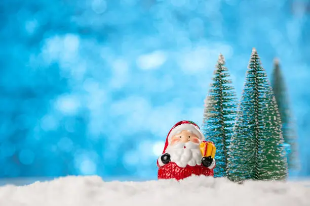 Photo of Winter background with Christmas trees and toy Santa Claus on a snow.