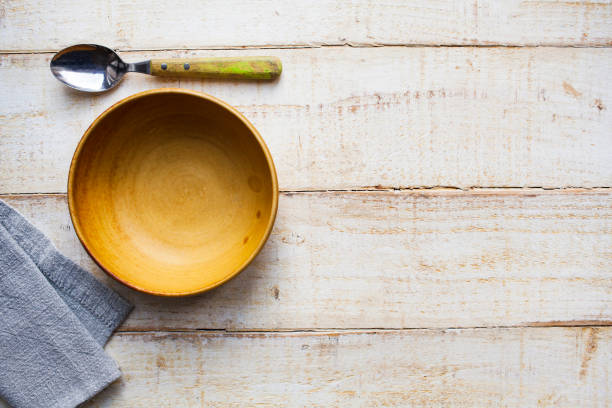 istock Empty yellow bowl, with a spoon and grey napkin, on a rough wooden surface viewed directly above with copy space 1292776014