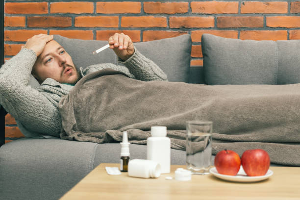 istock Sick man on sofa measure body temperature, check a thermometer, guy is diseased and feels badly ill, infection coronavirus, covid-19 or flu illness 1292776134
