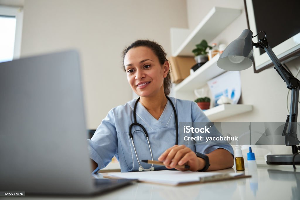 Doctor clicking on a laptop before her Woman watching a laptop screen while stretching her hand and typing on it Doctor Stock Photo
