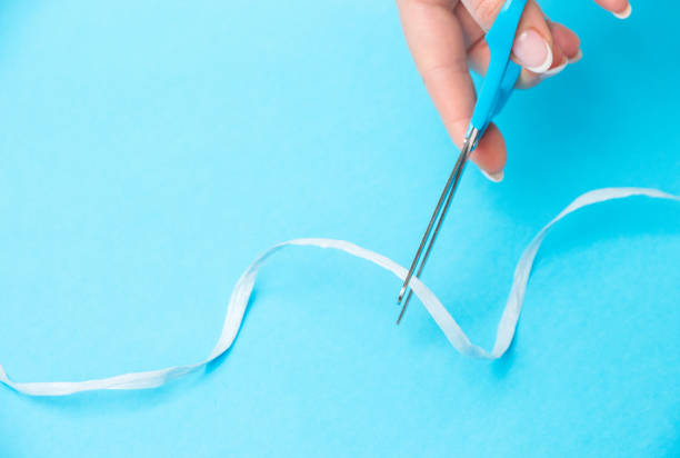 istock Woman's hand cuts ribbon with scissors on blue background 1292778623