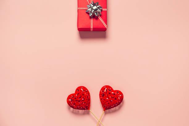 istock Abstract composition with two decorative hearts and red present box on pink paper background. 1292780657