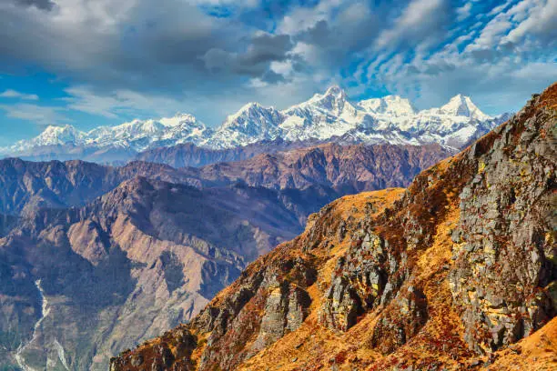 Rocky colorful mountain view of Himalayas with snowy Manaslu Himal peak and yellow rock in foreground with blue picturesque cloudy sky, Langtang, Nepal