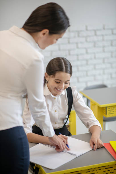 istock Schoolgirl writing and teacher helping in class 1292782948