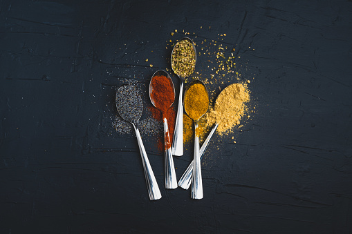 Spices in metal spoon on black background