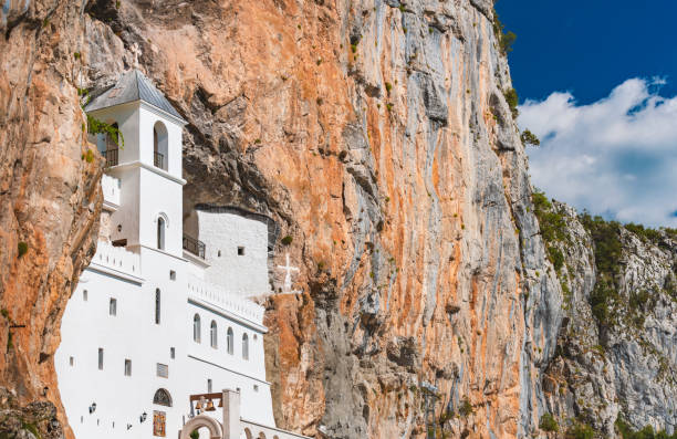 ostrog do mosteiro branco da igreja ortodoxa sérvia situada contra uma montanha quase vertical com céu azul nublado ao fundo. viagem de montenegro, europa. - ostrog - fotografias e filmes do acervo