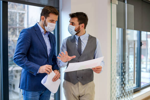 istock Two young colleges talking about paperwork beside window with their protective masks on. COVID-19 is dangerous. 1292790737