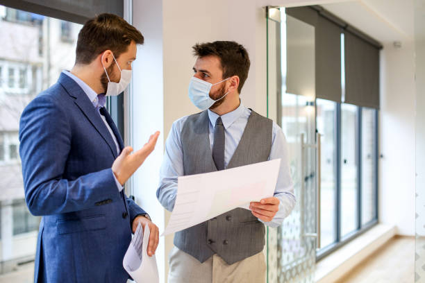 istock Two young businessmen standing by window with protective masks on. Corona awareness. 1292790740