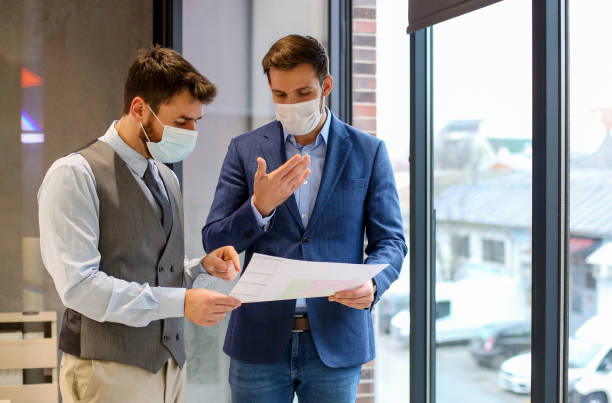 istock Two colleagues looking on printed charts,  wearing protective masks on. 1292791547