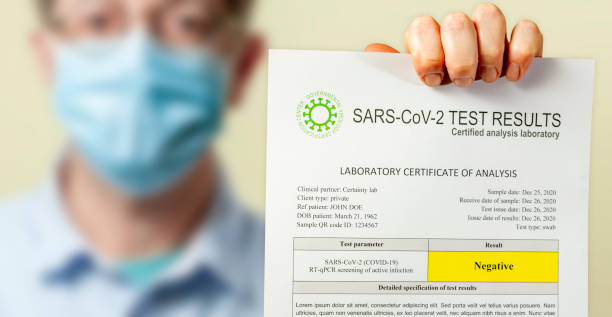 Man wearing protective surgical face mask holds up a negative test result document for SARS-CoV-2 coronavirus causing COVID-19 stock photo