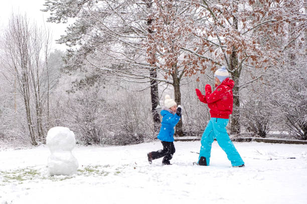 kaukasische mädchen mit einem kind, ein mädchen von 5 jahren, spielen und werfen schneebälle. winter fröhliches wochenende mit der familie. - child winter snow 4 5 years stock-fotos und bilder
