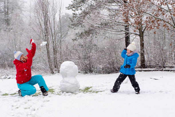 kaukasische mädchen mit einem kind, ein mädchen 5 jahre alt, machen einen schneemann im hof ihres hauses und spielen schneebälle. - child winter snow 4 5 years stock-fotos und bilder