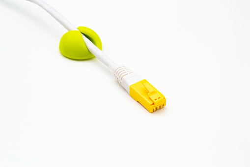 Computer network cable with yellow RJ-45 connector in green cable clip on white background