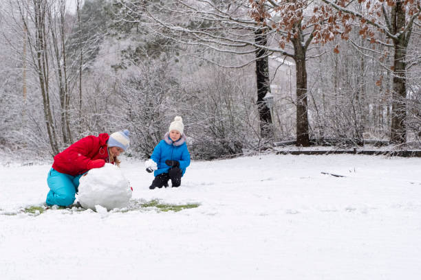 kaukasische mädchen mit einem kind, ein mädchen 5 jahre alt, machen einen schneemann im hof ihres hauses. - child winter snow 4 5 years stock-fotos und bilder