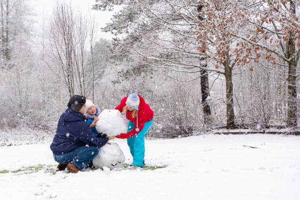 eine kaukasische familie mit einem kind macht einen schneemann. mama, papa und tochter sind 5 jahre alt. - child winter snow 4 5 years stock-fotos und bilder