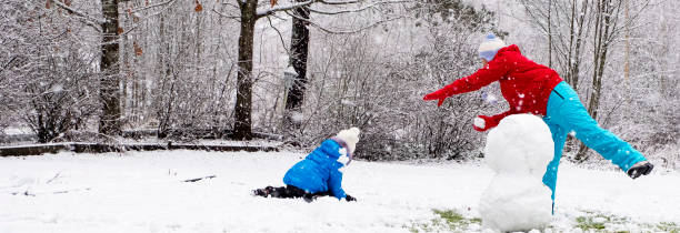 kaukasische mädchen mit einem kind, ein mädchen 5 jahre alt, machen einen schneemann im hof ihres hauses und spielen schneebälle. - child winter snow 4 5 years stock-fotos und bilder