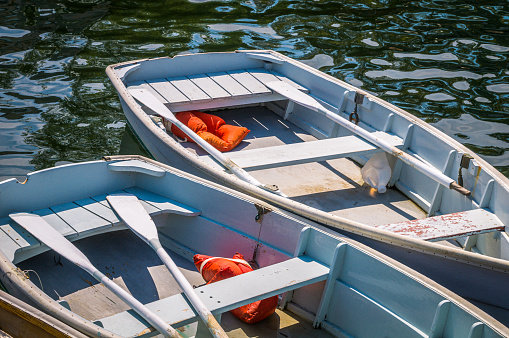 Two similar grey wooden rowboats with oars and orange life vests docked at a pier on Cape Cod.