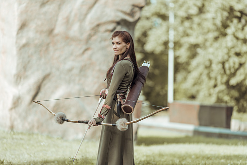 Archery woman with bow shooting on the forest