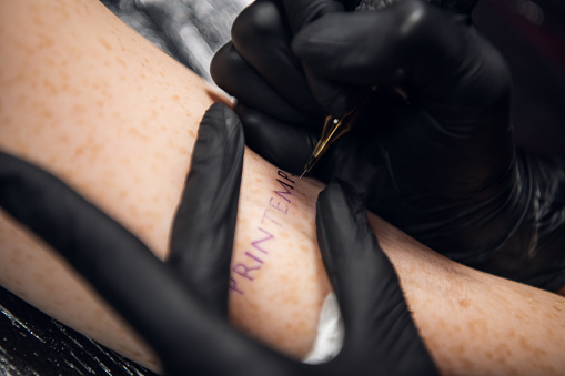 Close-up stick and poke method of tattooing a young girl's hand with the inscription in French printemps -- spring