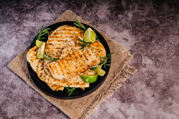 grilled chicken fillet on a black plate with lime pieces and fresh rosemary.grilled chicken fillet on a cooking pan - chicken breast chicken grilled chicken protein imagens e fotografias de stock