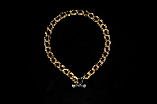 Golden jewelry chain with medallion isolated on black background.