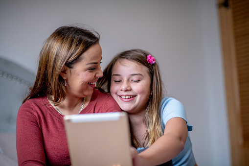A mother and daughter duo are using their tablet to video call their family members who are living far away. They appear to be happy and excited to talk to them.