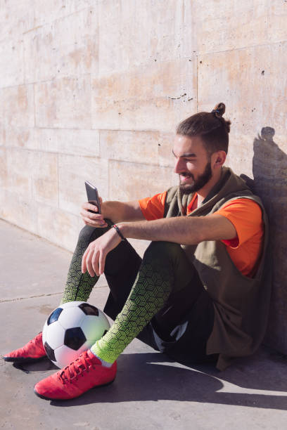 fußballer ruhe beratung sein handy - soccer player soccer men smiling stock-fotos und bilder