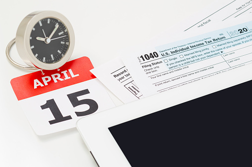 April 15 Tax Day concept - tablet screen, calendar, clock and 1040 tax return.