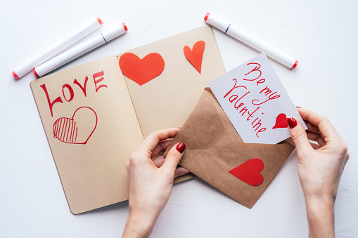 Female hands put a written valentine in an envelope. Declaration of love and a holiday surprise.