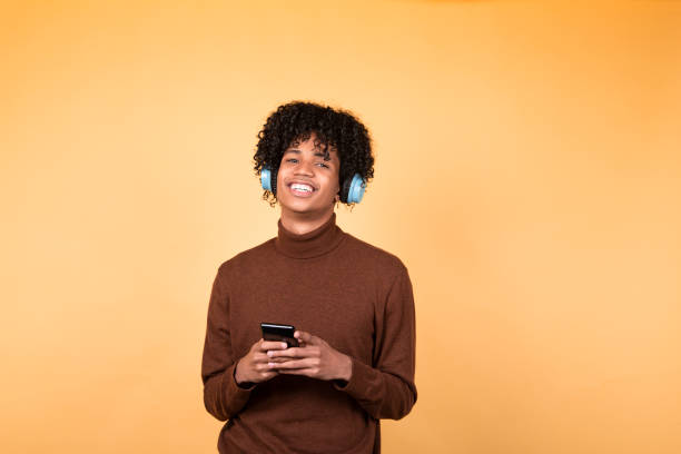 istock Young afro hair man standing in poses isolated on yellow background using mobile phone device, writes text messages on modern smartphone, watches funny videos during free time 1292860315