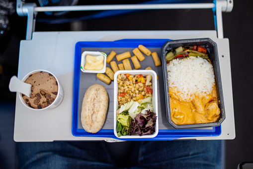 Ice cream, rice, salad, yellow sauce, and pudding on gray and blue tray from above. Top view of fresh airplane complete meal above small table. Plane food