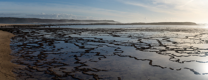 A panorama view of golden evening light reflectiing in tidal pools on a rocky beach with the ocean behind