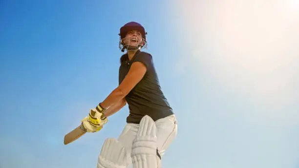 Female cricket player playing cricket on ground against sky.