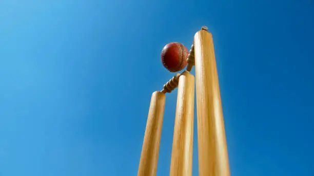 Close-up of cricket ball hitting the stumps and knocking off the bails against sky.