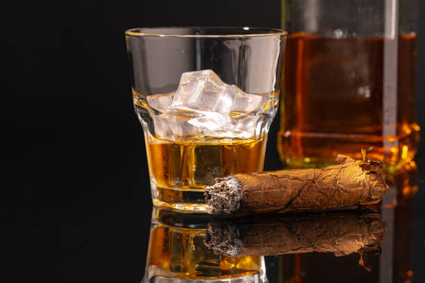 istock Glass of whisky and lighted cigar on black background 1292880559