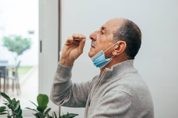 Senior man using an nasal swab for covid 19 detection. Senior man sitting, self test for COVID-19 at home with Antigen test kit. Coronavirus nasal swab test for infection. Medicine and health-related services online. antigen stock pictures, royalty-free photos & images