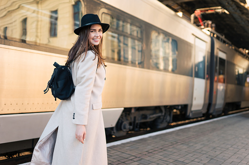 Beautiful girl tourist rushes to the train. Young cheerful woman walks along the platform of the station and look back