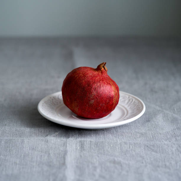 istock Still life with whole pomegranate on plate on table covered with crumpled gray tablecloth, in natural 1292885867