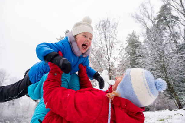 若い女性が雪の中に横たわり、娘の5歳の女の子を抱いています。少女は幸せそうに微笑む。白人の家族は屋外で冬に楽しんでいます。 - 35 40 years ストックフォトと画像