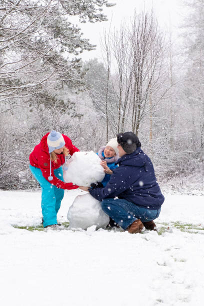 семья с ребенком, девочка 5 лет кавказка. семья делает снеговика. весело и весело по выходным зимой. - 35 40 years стоковые фото и изображения