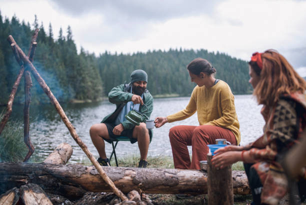 istock Young Cheerful And Smiling People Are Having Fun On Their Camping Vacation While Drinking Tea Next To The Camp Fire 1292903451