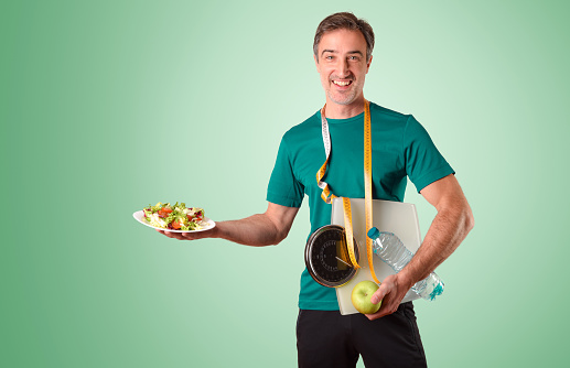 Man dressed in sportswear with meter scale and water and salad plate on green isolated gradient background