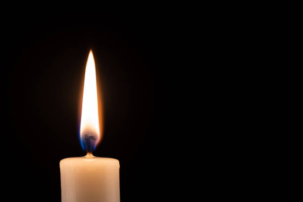 Photo of Burning candle in front of a black background with place for text.