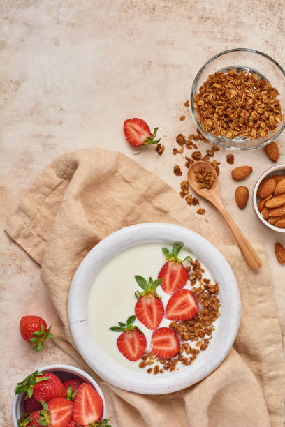 istock Greek yogurt in white bowl with ingredients for making breakfast granola and fresh strawberries on old beige table. Top view. 1292906276