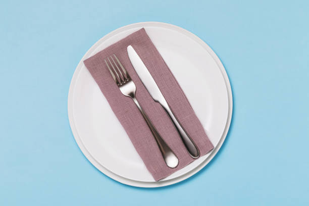 istock Cutlery and napkin in a white ceramic plate on a blue background, top view 1292911409
