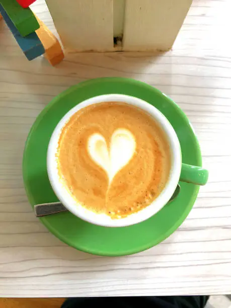 Simple flatwhite heartshaped coffee art on a green saucer