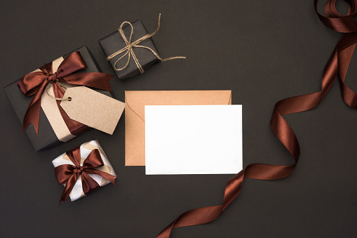 Gift boxes wrapped in kraft paper with brown ribbon and bow on black background. Gifts for men concept. Father's day greeting card, festive decor. Top view with copy space. Flat lay.