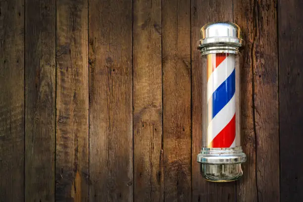 Photo of Barber pole. Barbershop pole on a wooden background with copy space.