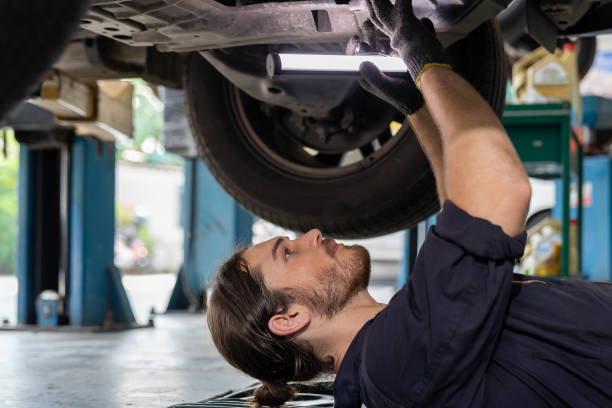 istock Male car mechanic worker working using wrench tool for repair, maintenance underneath lifted car. Mechanic vehicle service checking under car in garage. Auto car repair service, maintenance concept 1292923442